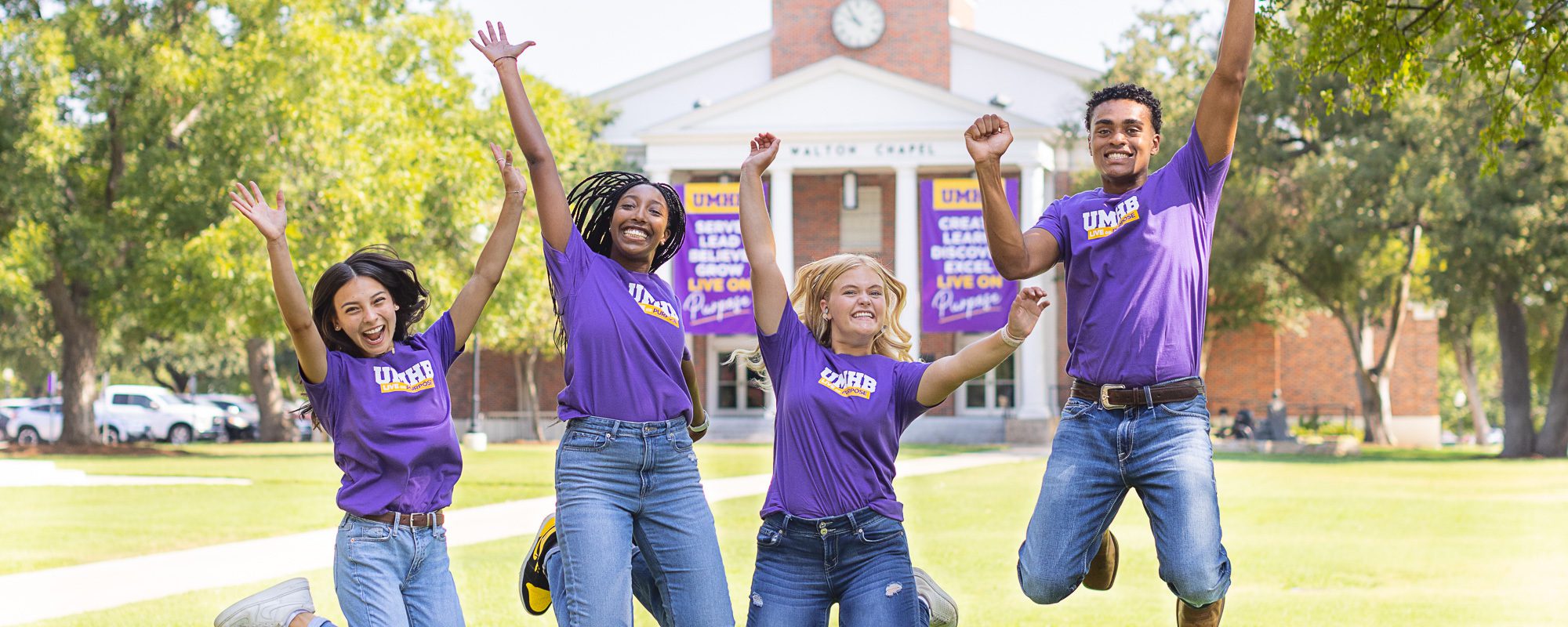 Student life students jumping in the air in front of walton chapel wearing t-shirts with live on puprose offical brand at UMHB.